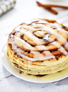 a stack of pancakes covered in icing on top of a white plate next to cinnamon sticks