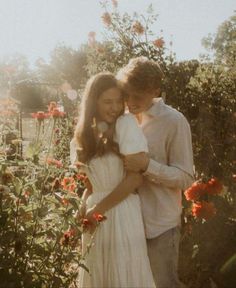 a man and woman standing next to each other in a field of flowers with the sun shining on them