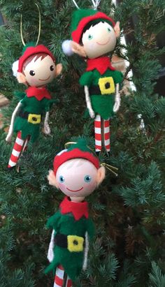 three elf ornaments hanging from a christmas tree