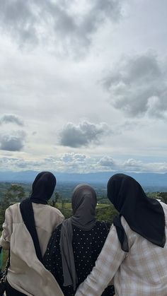 two women sitting on top of a hill looking out at the valley and clouds in the sky