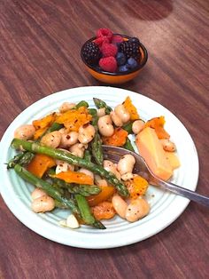 a white plate topped with asparagus, carrots and chickpeas next to a bowl of berries