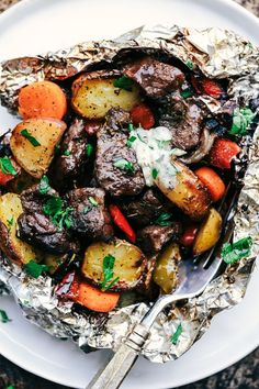 two foil packets filled with meat, potatoes and carrots on top of a table