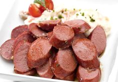 a white plate topped with sliced sausage next to mashed potatoes