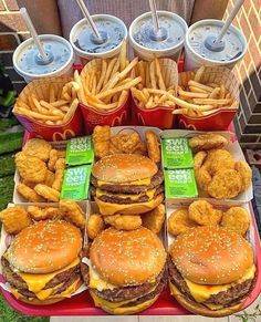 a table topped with lots of hamburgers and fries next to cups of soda on top of each other