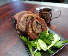 bacon wrapped meat on a black plate next to celery and a cup of tea