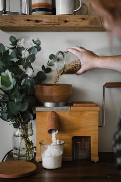 a person pouring something into a blender on top of a wooden table next to a potted plant