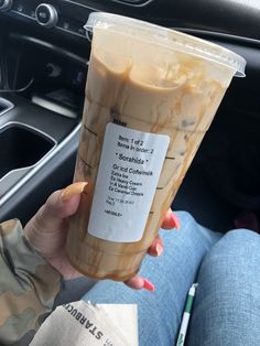 a woman holding up a drink in her hand while sitting in the drivers seat of a car