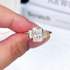 a woman's hand holding an engagement ring with three baguettes