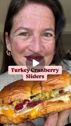 a woman holding a large sandwich in her hand with the words turkey cranberry sliders on it