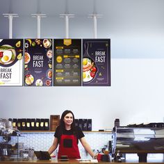 a woman sitting at a counter in front of a breakfast fast food restaurant with menus hanging from the ceiling