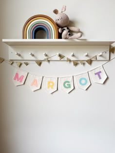 a white shelf holding a stuffed animal and some pennants with the word margot on it