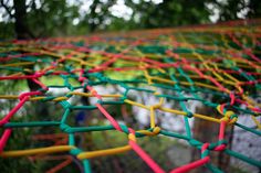 the colorful net is made up of many different colored sticks and plastic pegs, with trees in the background