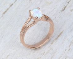 a gold ring with a white opal in the center on top of a piece of wood