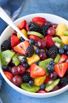 a white bowl filled with fresh fruit on top of a blue table cloth next to a spoon