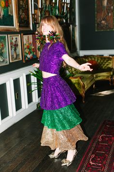 a woman in a purple and green dress standing on a wooden floor next to a rug