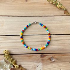 a bracelet with multi colored beads on a wooden table next to dried flowers and leaves