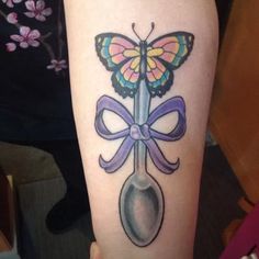 a tattoo with a spoon and butterfly on the side of her leg, which has a purple ribbon around it