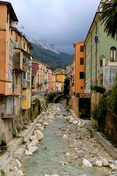 a river running through a small town next to tall buildings with mountains in the background