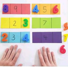 two hands are next to colorful numbers and numerals on a white surface with colored paper