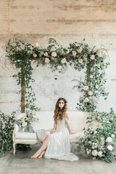 a woman sitting on top of a white couch next to a wall covered in greenery