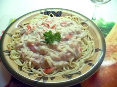 a plate of pasta with sauce and vegetables on it next to a glass of wine