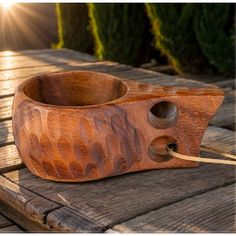 a wooden bowl sitting on top of a wooden table next to some bushes and trees