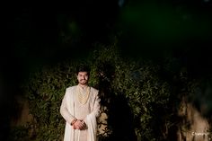 a man in a white outfit standing next to a bush and bushes at night time