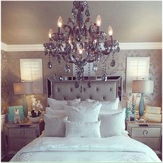 a bedroom with a chandelier hanging over the bed and pillows on the floor