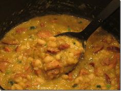 a ladle full of beans and meat in a pot with a black spoon inside