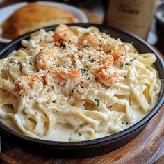 pasta with shrimp and parmesan cheese in a bowl on a wooden table next to bread