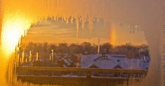 a window with icicles on it and a rainbow in the sky behind it at sunset