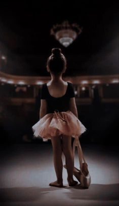 a young ballerina standing in front of an empty stage with her ballet shoes on