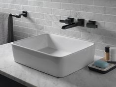 a white square sink sitting on top of a counter next to a towel rack and soap dispenser