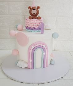 a birthday cake with a teddy bear sitting on the top of it and a rainbow arch