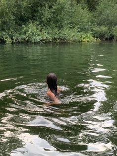 a woman is swimming in the water with trees in the backgrouds and bushes behind her