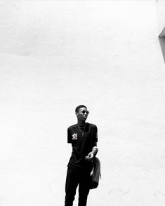 a man standing in front of a white wall holding a bag and looking at the camera