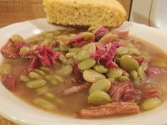 a white plate topped with meat and bean soup next to a piece of cornbread