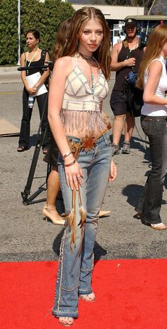 a woman standing on top of a red carpet wearing jeans and fringed boots with her hands in her pockets