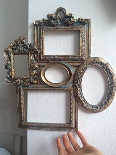 a hand is reaching up to an ornate gold frame with four smaller frames on the wall