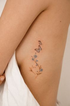 a woman's back with flowers and butterflies tattooed on her left side ribcage