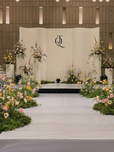 an outdoor ceremony with flowers and greenery on the side walk, in front of a large screen