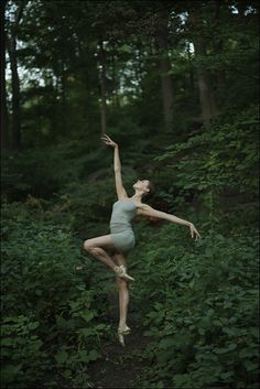 a woman is dancing in the woods with her arms stretched out and legs spread wide