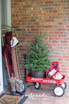 a christmas tree sitting on top of a red wagon next to a brick wall and door