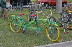 several bicycles are parked on the grass near trees and people standing around them with cars in the background