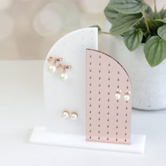 two pairs of pearl earrings are on a white stand next to a potted plant