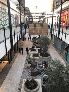 an indoor shopping mall with plants and people walking around the walkways on either side