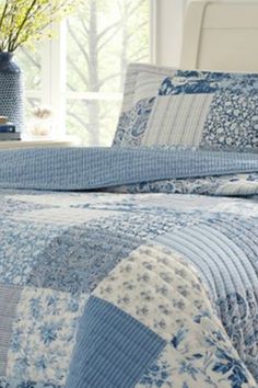 a blue and white quilted bedspread with flowers in a vase next to it