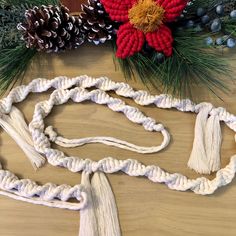 a white rope with tassels next to pine cones and christmas decorations on a wooden table