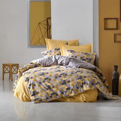 a bed with yellow sheets and pillows in a room next to a mirror on the wall