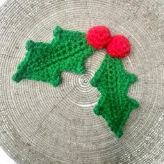 two crocheted holly leaves with red berries on them sitting on top of a basket